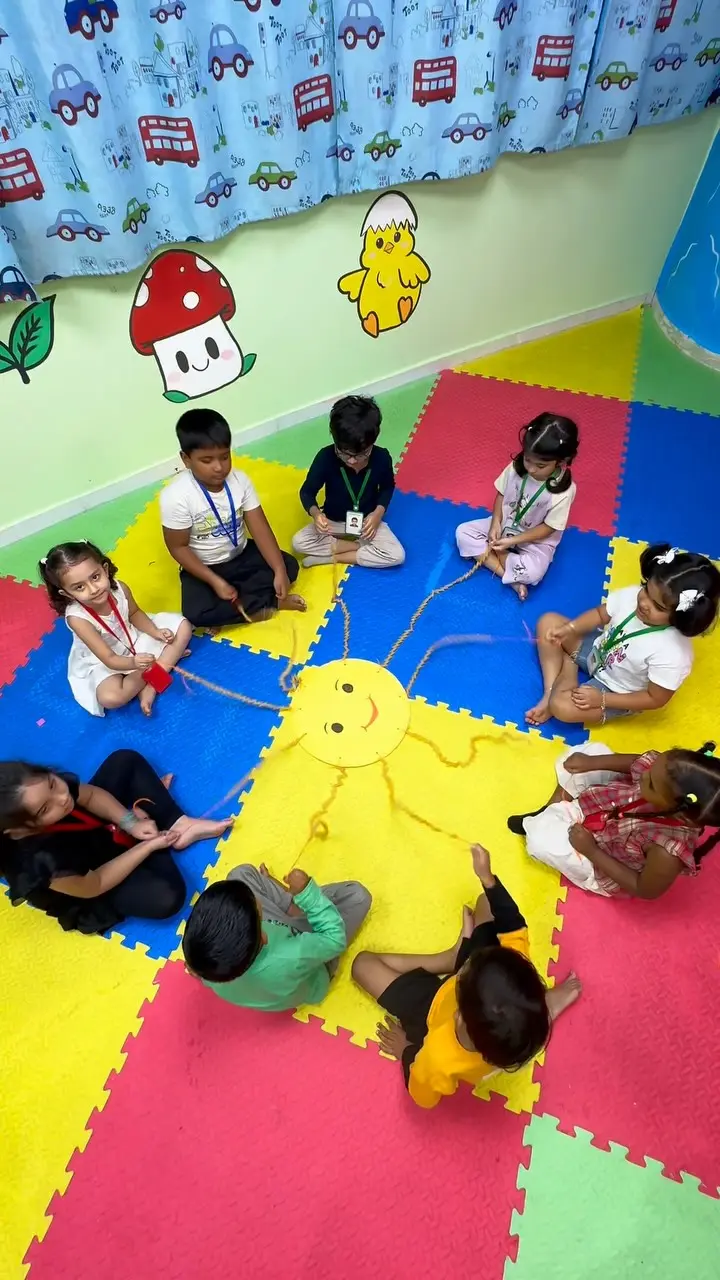 Children seated in a circle on the play mats around a yellow rope sun