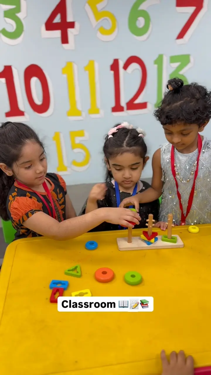 Children choosing wooden shapes at a table in front of the painted numbers wall