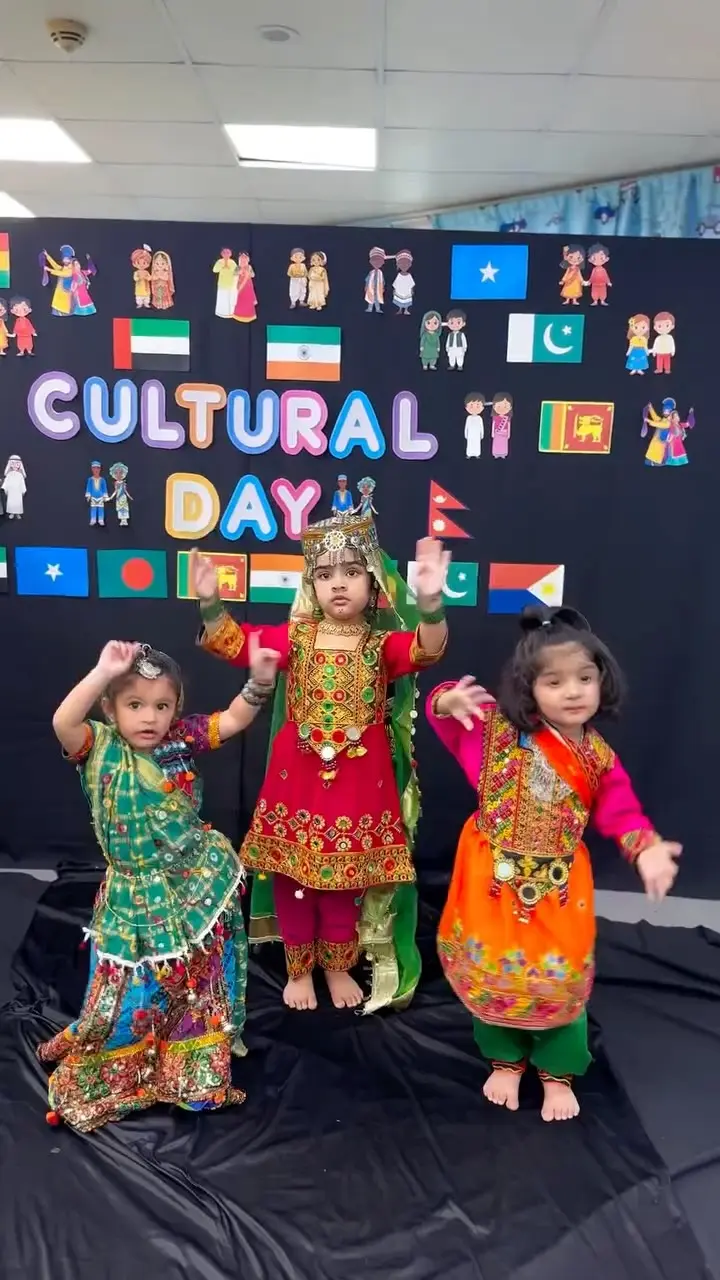 Children in traditional dress in front of the Cultural Day flags board