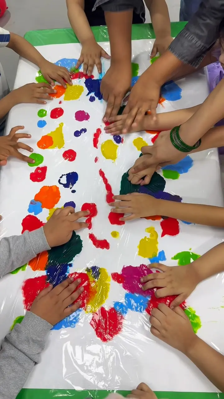 Many small hands spreading bright paint across a table, seen from above