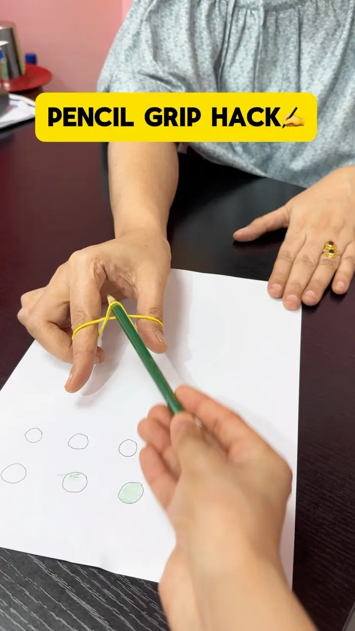 An adult hand showing a pencil grip with a rubber band on a worksheet