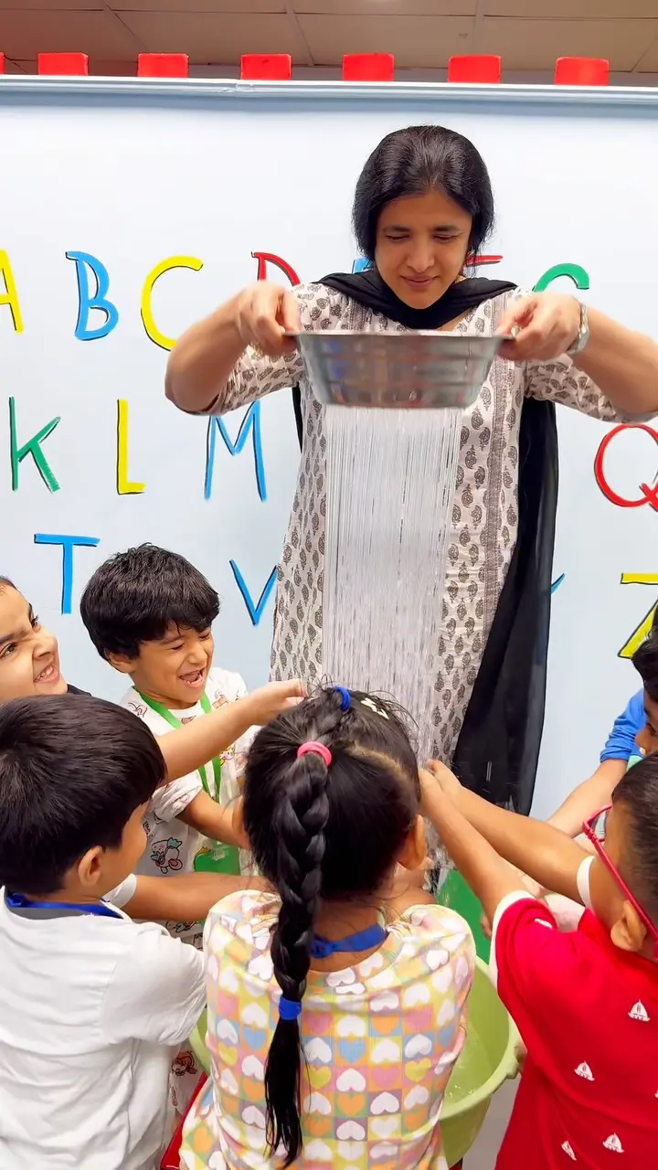 Children reaching up as a teacher makes rain with a colander