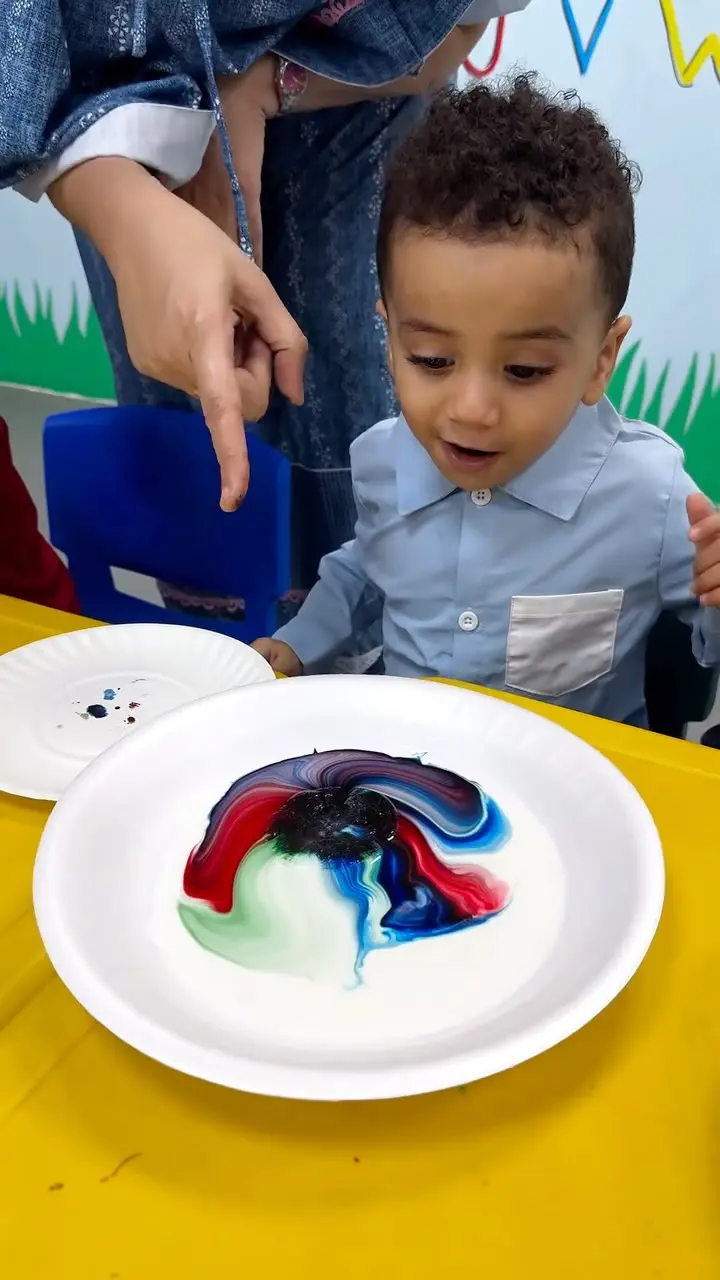 A child watching colours spread across a plate of milk