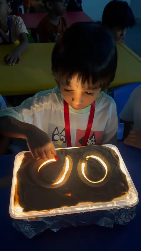 A child tracing letter shapes in a lit sand tray