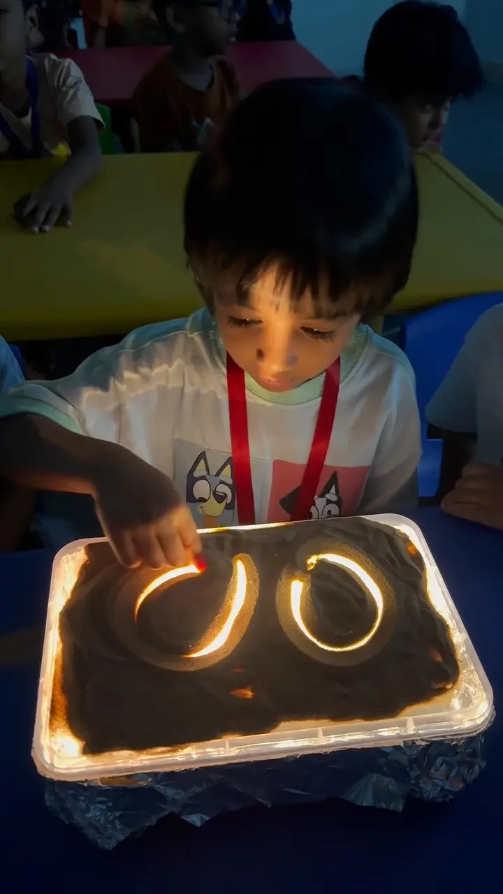 A child tracing letter shapes in a lit sand tray