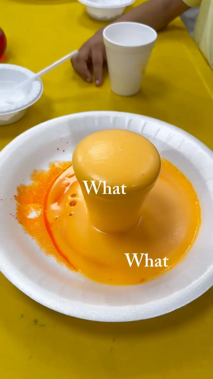 A baking-soda volcano erupting with orange foam on a plate